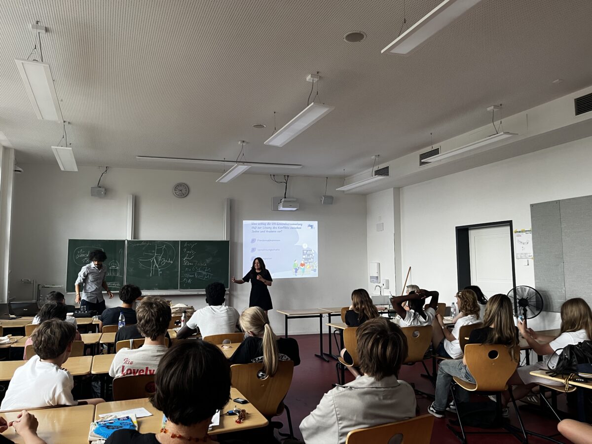 Lehrerin mit neutralem Blick in schwarzer Kleidung vor Projektion im Klassenraum