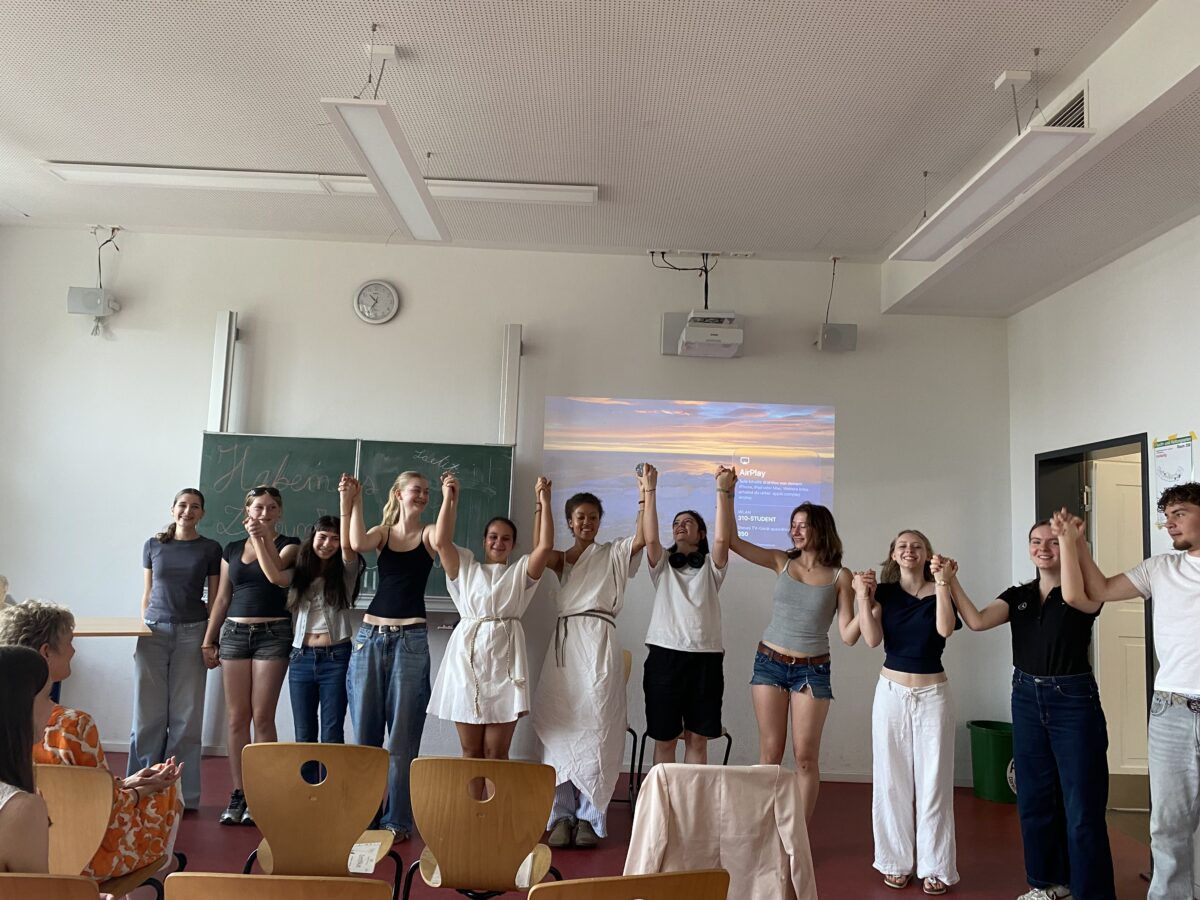 Gruppe Jugendlicher jubelt lächelnd in bunten Outfits vor Beamerbild