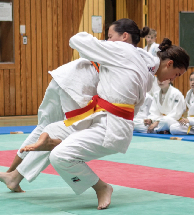 Zwei konzentrierte Judokas in weissen Anzuegen kaempfen auf der Matte