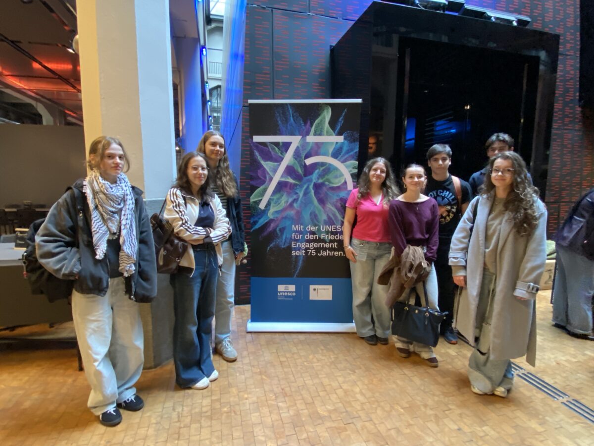 Laechelnde junge Gruppe steht neben einem UNESCO Banner zum 75 Jubilaeum