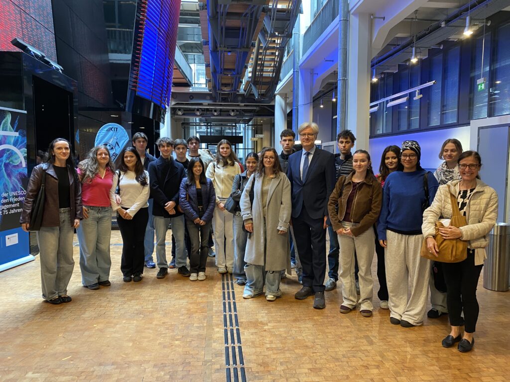 Eine laechelnde Gruppe junger Menschen mit einem Mann im Anzug in moderner Halle