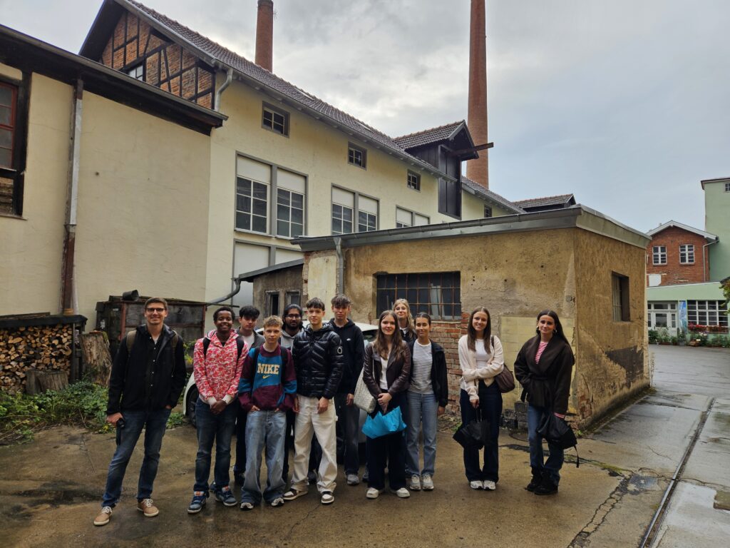 Laechelnde Gruppe junger Menschen vor alten Fabrikgebaeuden mit Schornstein
