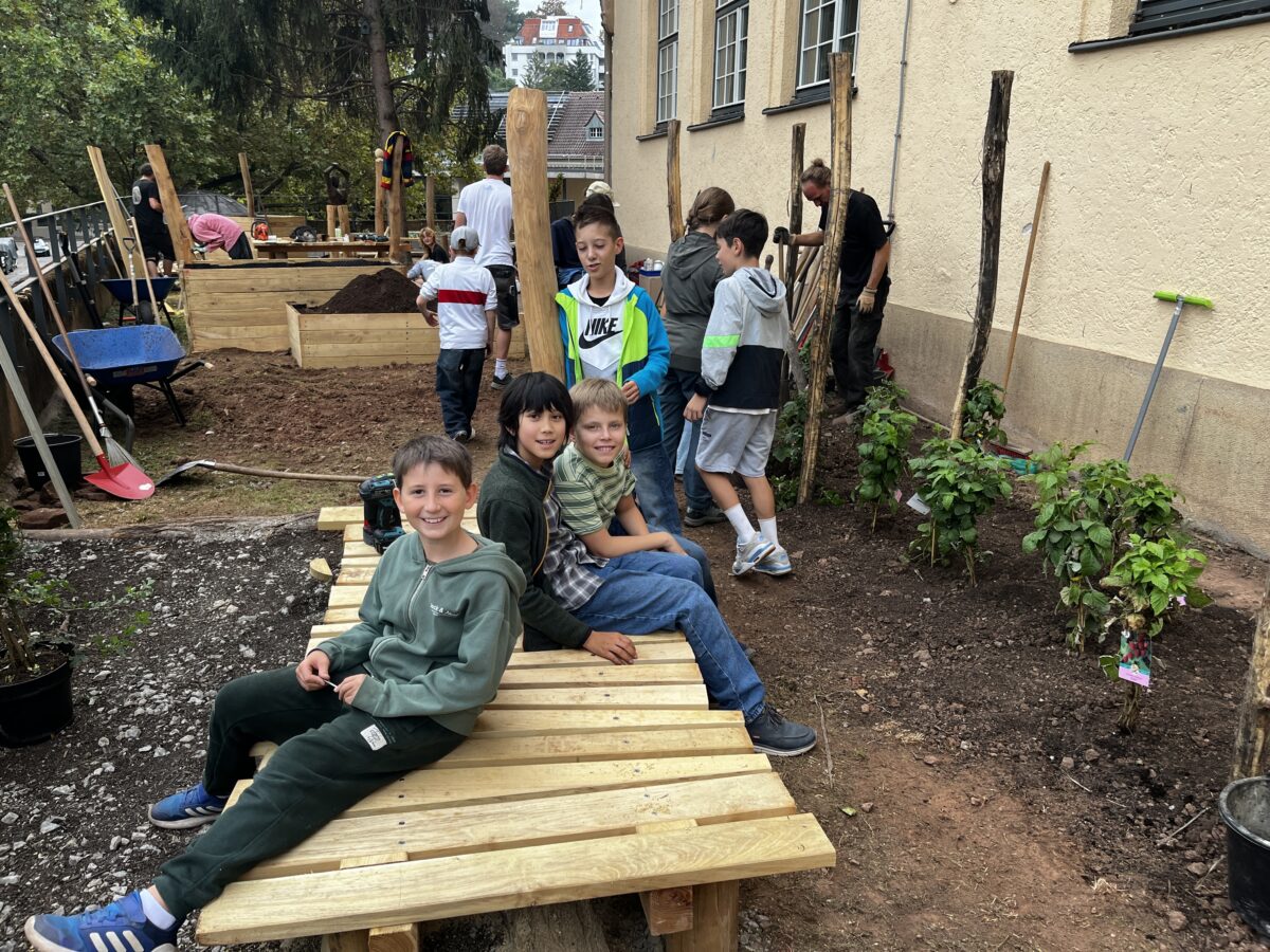 Drei laechelnde Jungen sitzen auf einer Holzbank im Garten bei Bauarbeiten