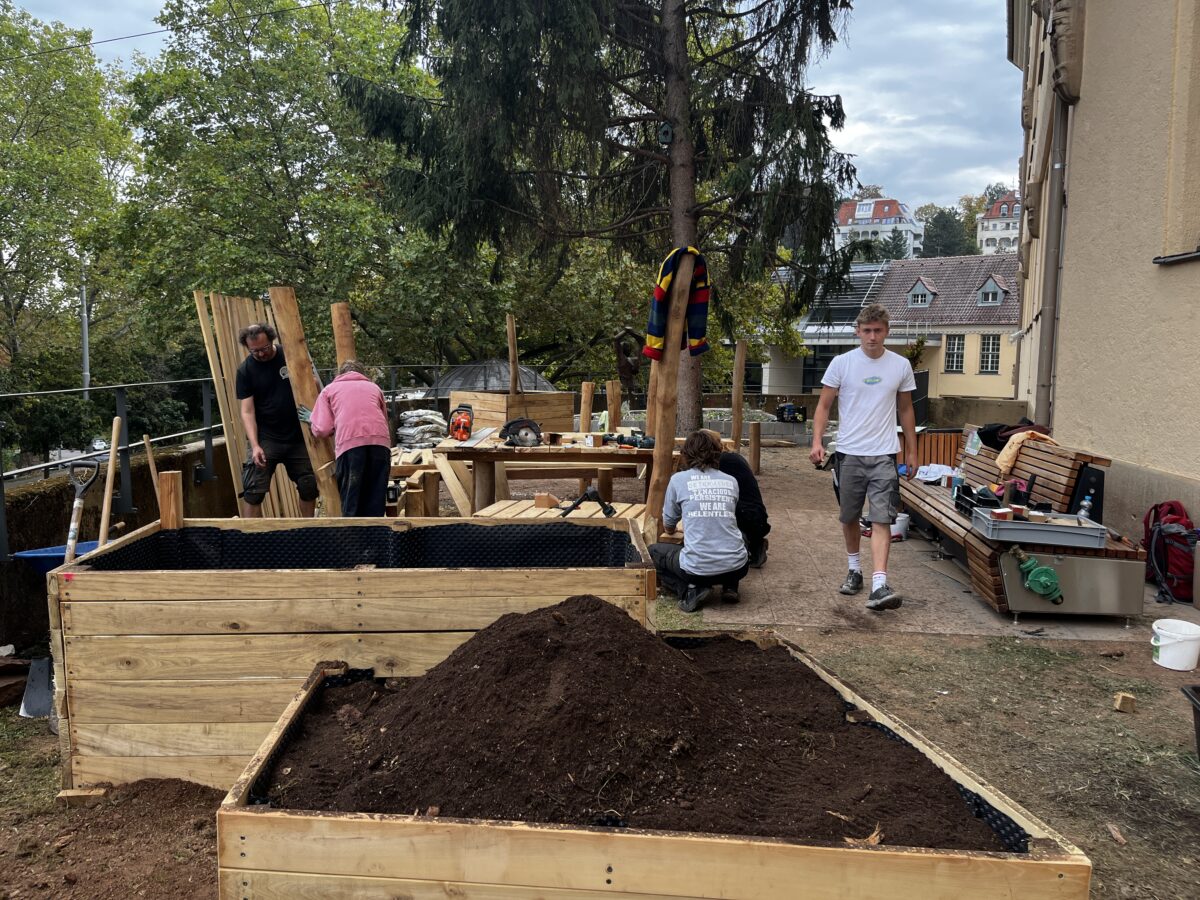 Menschen bauen Hochbeete aus Holz im Garten neben einem Erdhaufen