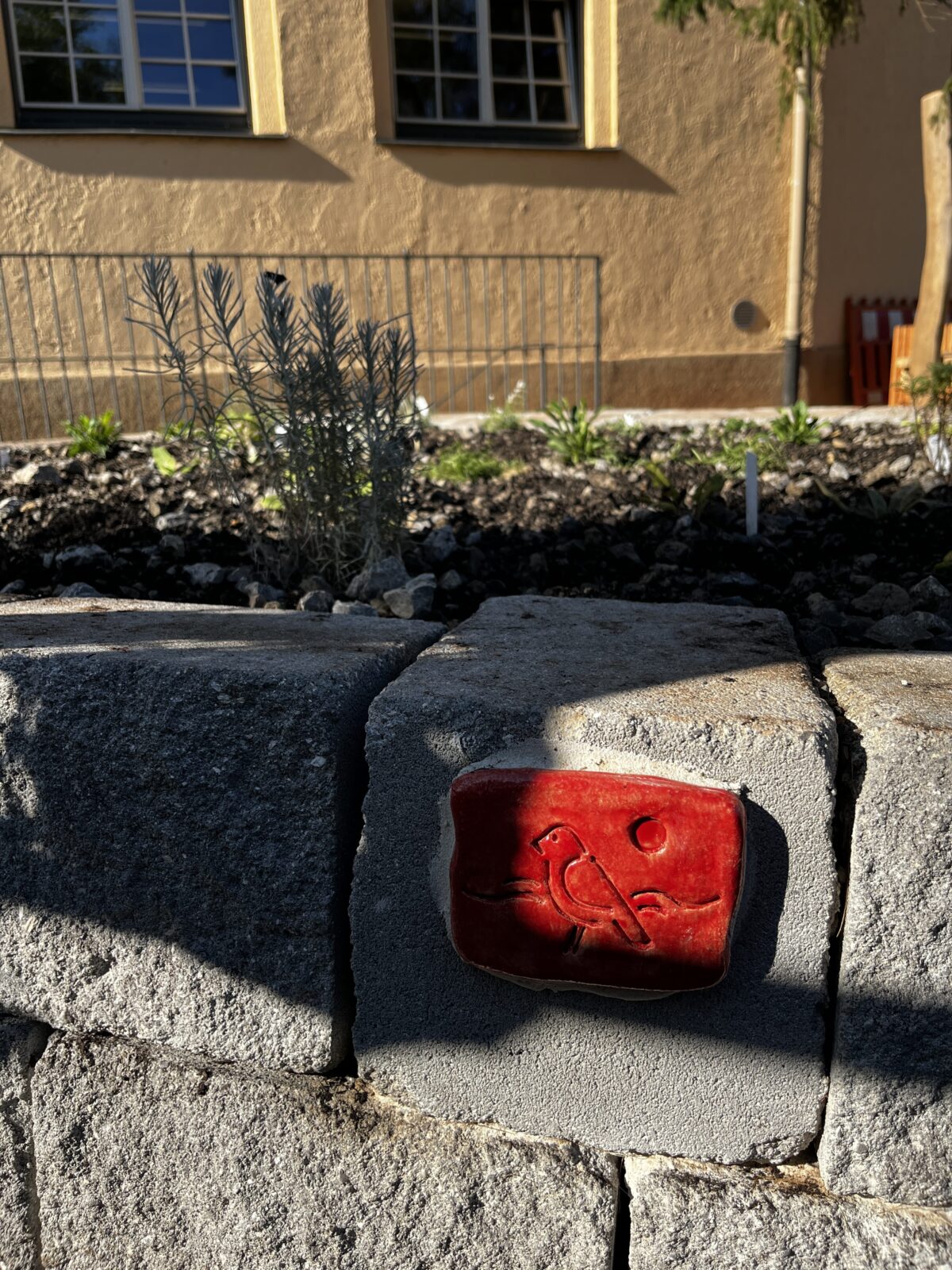 Rote Keramikfliese mit Vogelmotiv liegt auf einer Steinmauer im Sonnenlicht