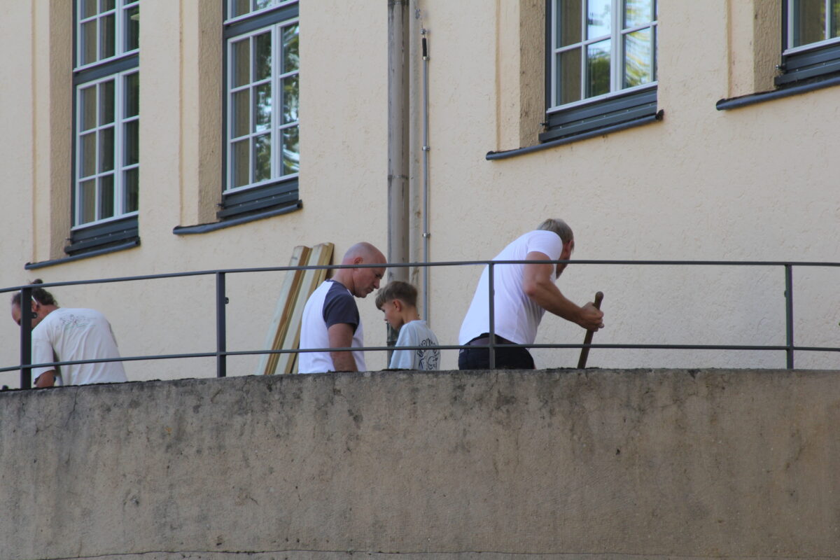 Drei Maenner und ein Junge in weissen Shirts arbeiten konzentriert an einer Mauer