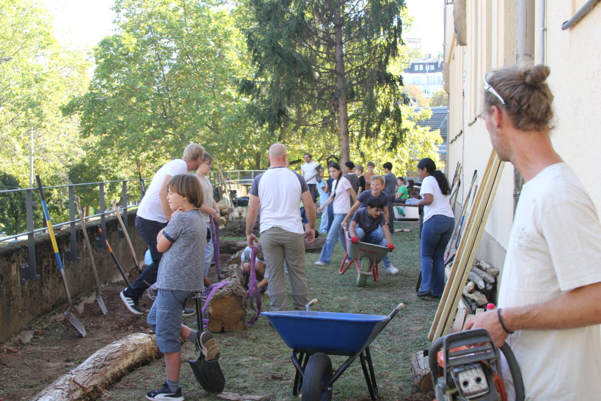 Kinder und Erwachsene arbeiten gemeinsam im Garten mit Schubkarren und Werkzeug