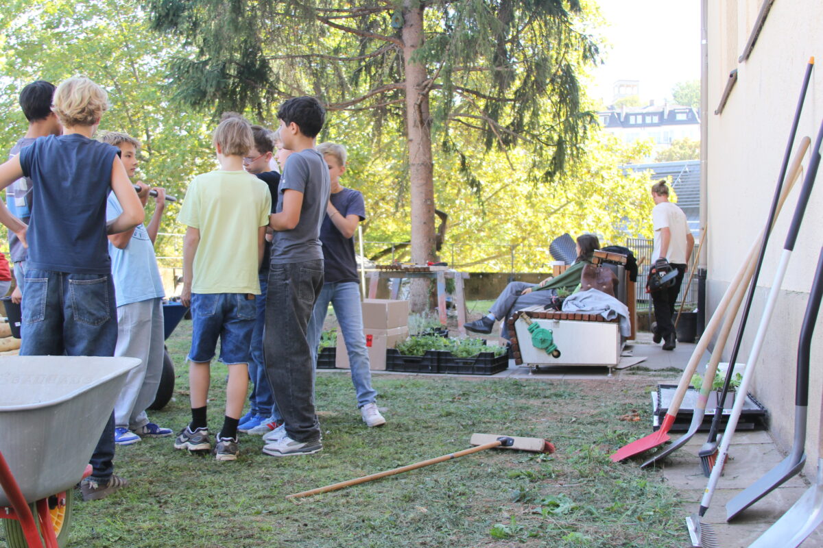 Eine Gruppe Jugendlicher steht bei Gartenarbeiten im sonnigen Hof zusammen