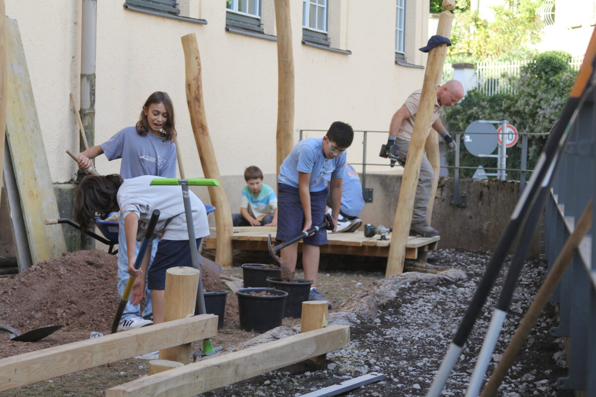 Kinder und ein Mann arbeiten konzentriert mit Werkzeugen an einer Baustelle