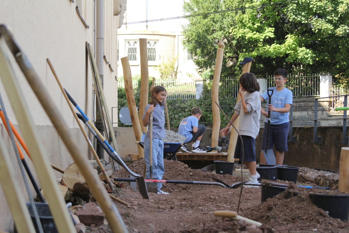 Vier Kinder in blauen Shirts arbeiten froehlich mit Werkzeugen im Garten