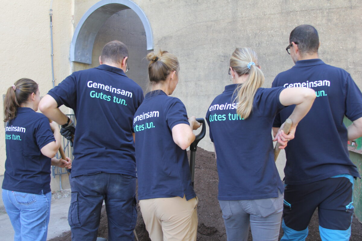 Fuenf Personen von hinten in blauen Shirts mit Aufschrift Gemeinsam Gutes tun