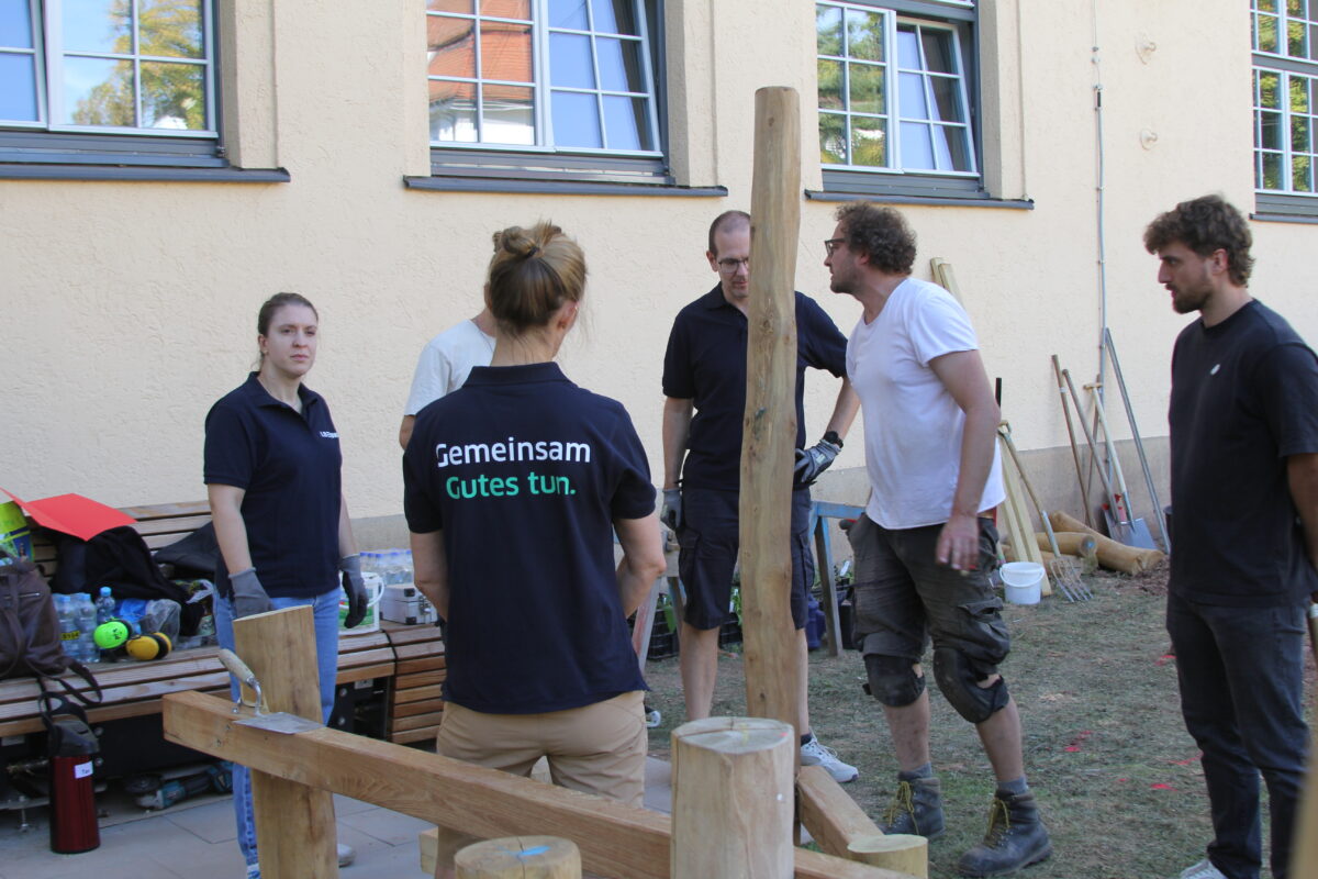 Gruppe von Helfern in dunklen Shirts arbeitet konzentriert an einem Holzprojekt