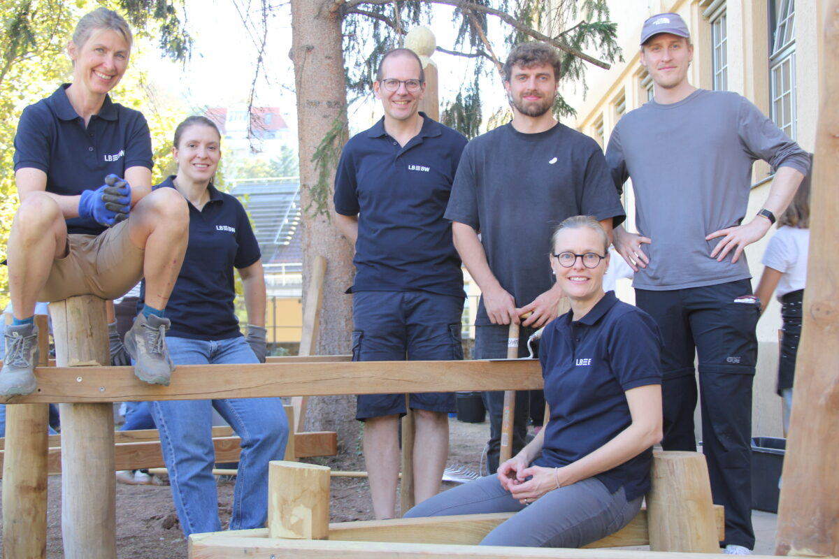 Sechs laechelnde Personen in dunkelblauen Poloshirts bei Gartenarbeit im Freien