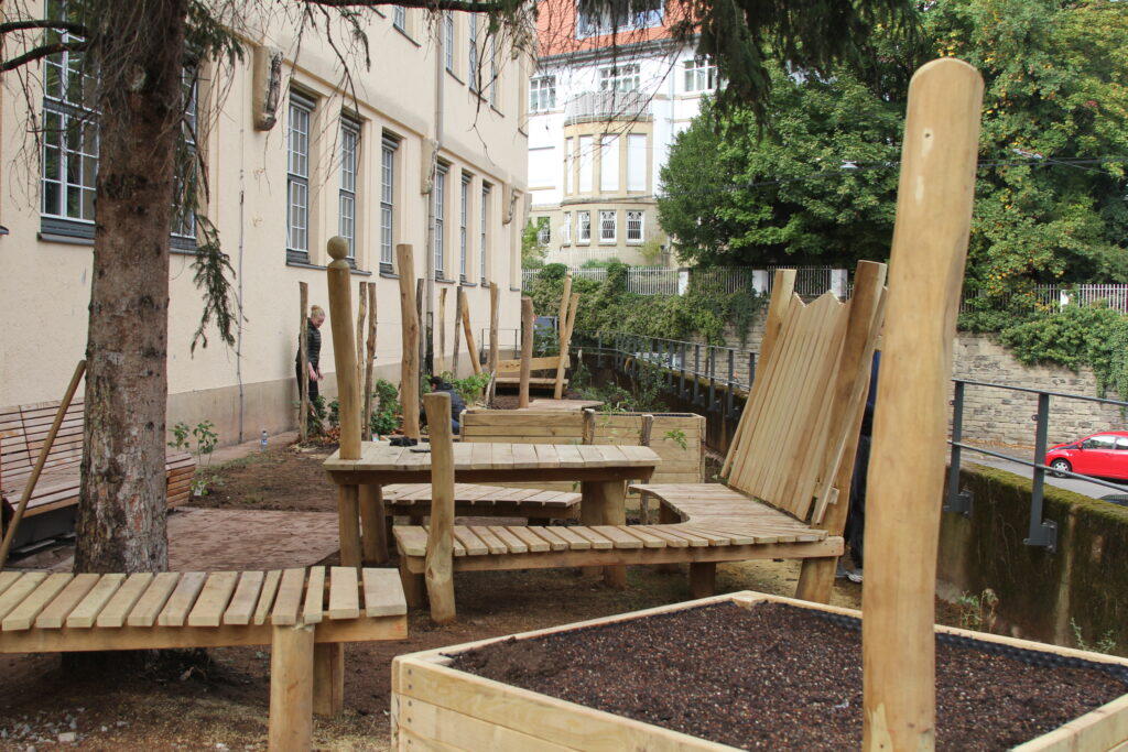 Neu gestalteter Schulgarten mit Holzbaenken und Hochbeeten vor einem Gebaeude