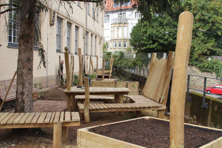 Neu gestalteter Schulgarten mit Holzbaenken und Hochbeeten vor einem Gebaeude
