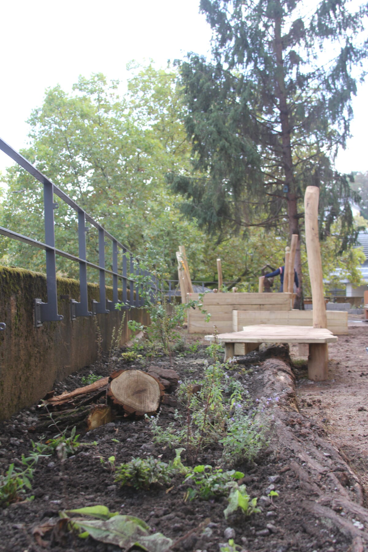 Ein naturnaher Spielplatz im Bau mit Holzelementen Baumstumpf und Metallgelaender