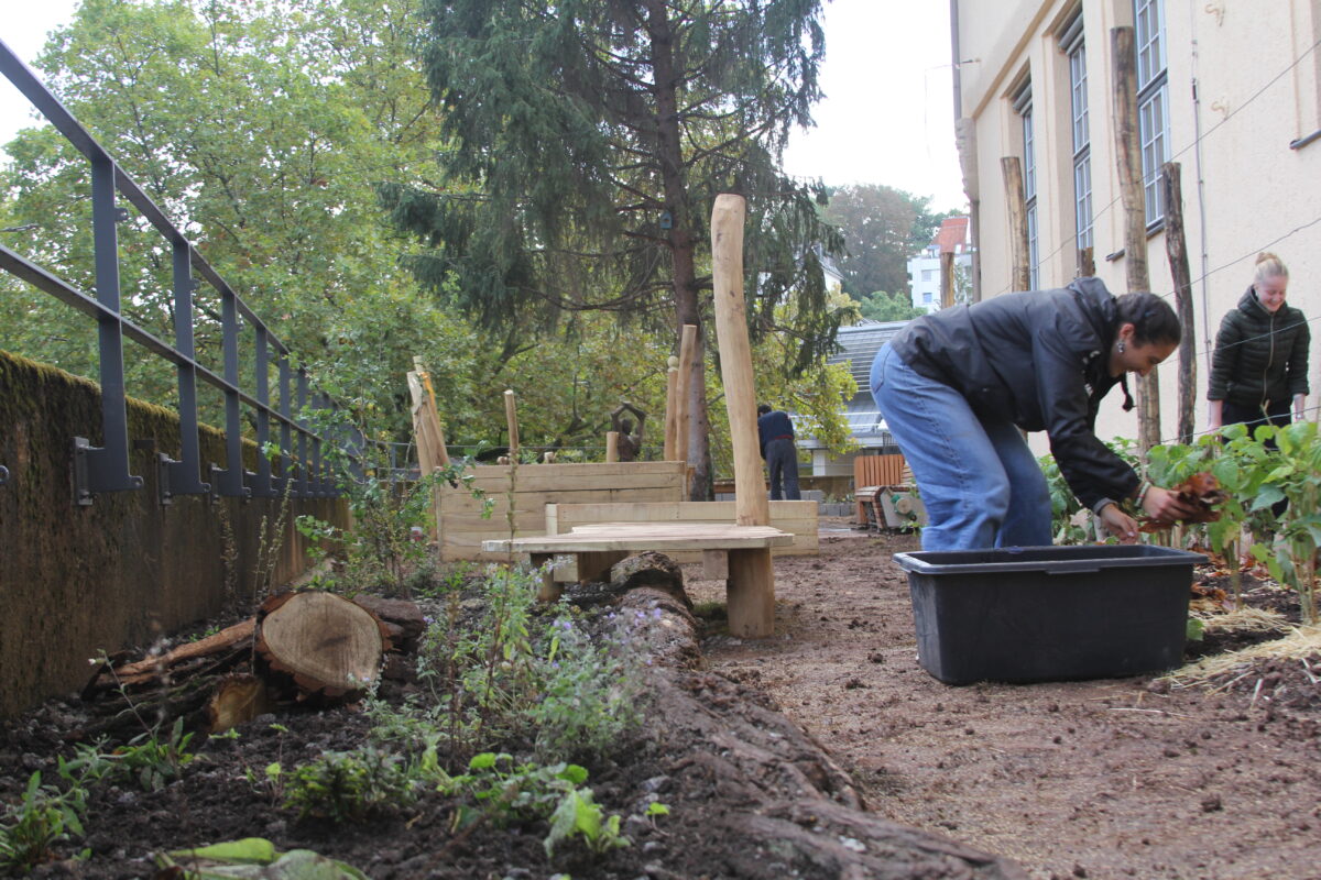 Menschen arbeiten konzentriert in einem naturnahen Garten neben einem Gebaeude