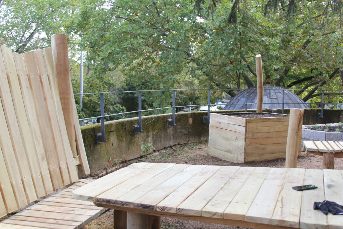 Ein neu gebauter Holztisch mit Hochbeet in einem Garten umgeben von Baeumen
